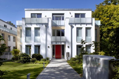 Modern white house with red door in front of a clear sky.