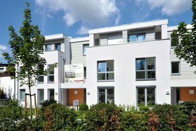 Modern apartment building with adjoining garden and shady trees.