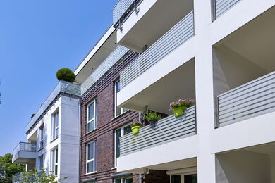 Modern apartment block with balconies decorated with potted plants and flowers, featuring a mix of brick and white façade under a clear blue sky.